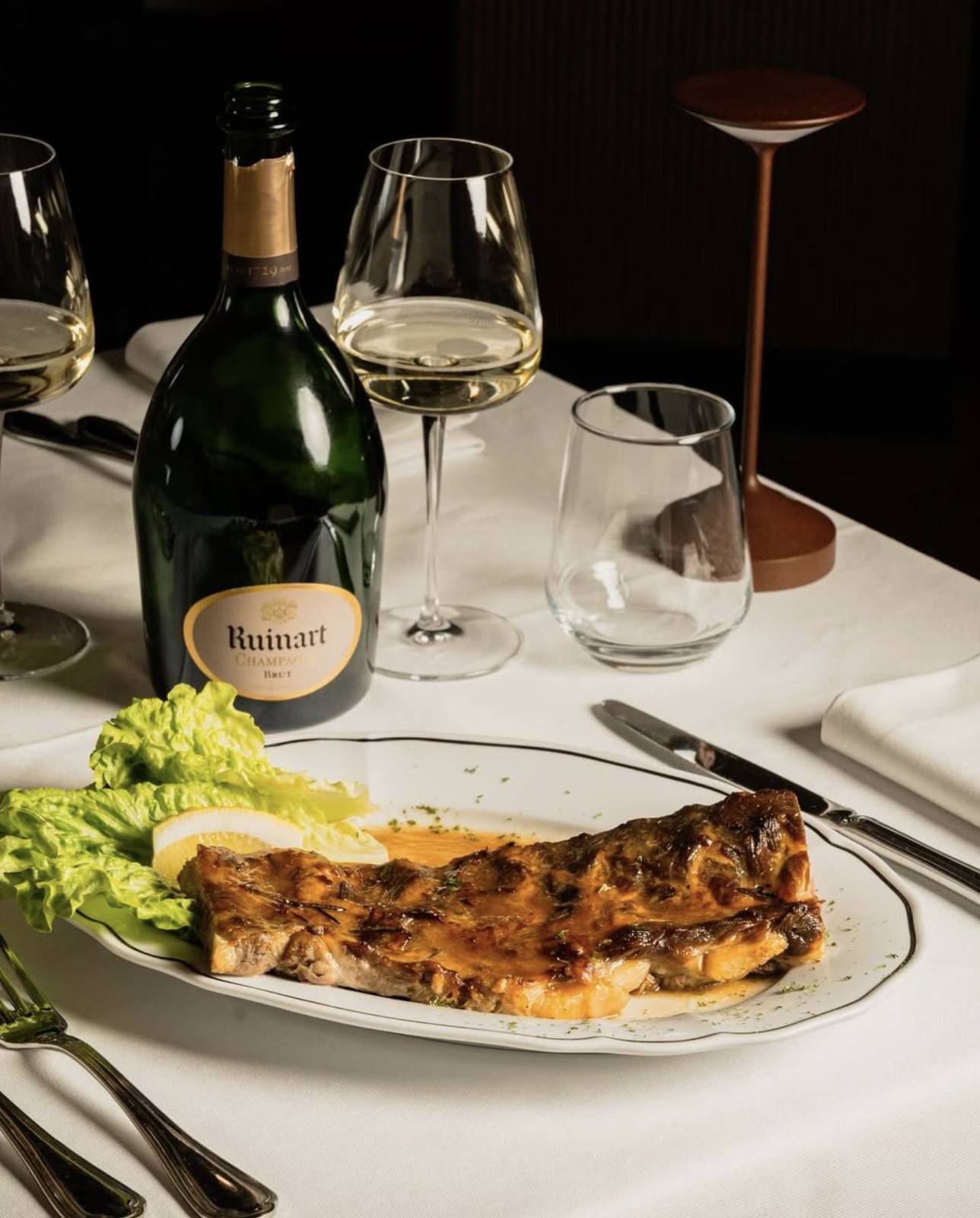 La tavola apparecchiata dell'Osteria Santa Chiara: tovaglia bianca, piatti a filo nero, champagne